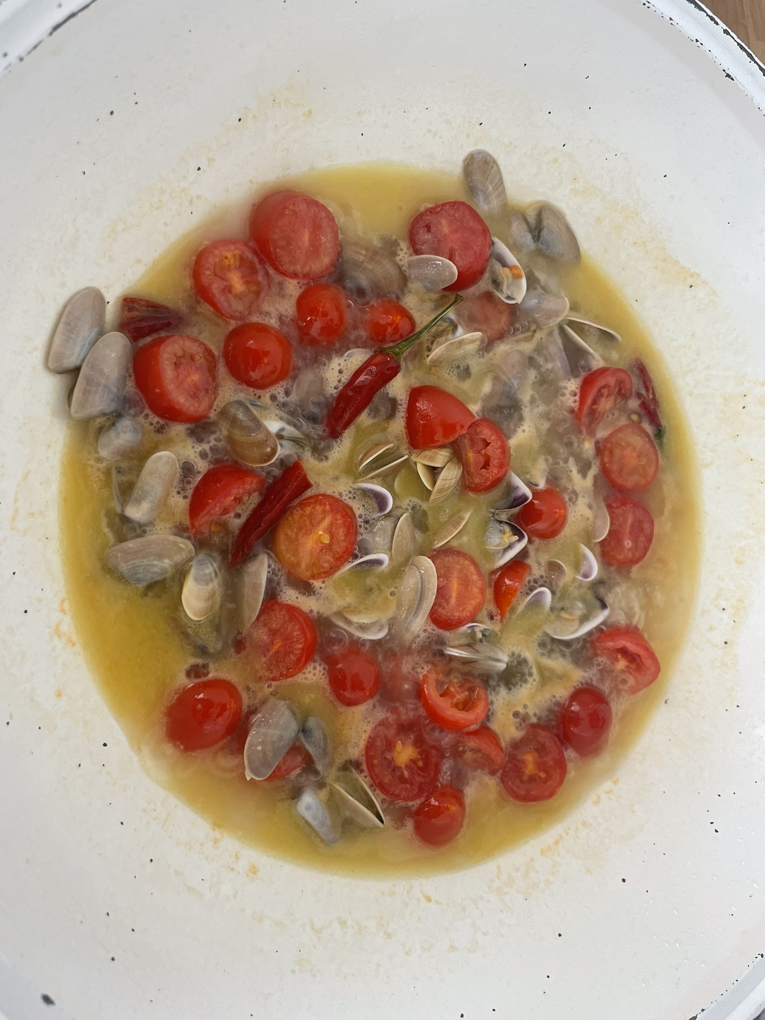 Clams and cherry tomatoes simmering in a white pan with chilli